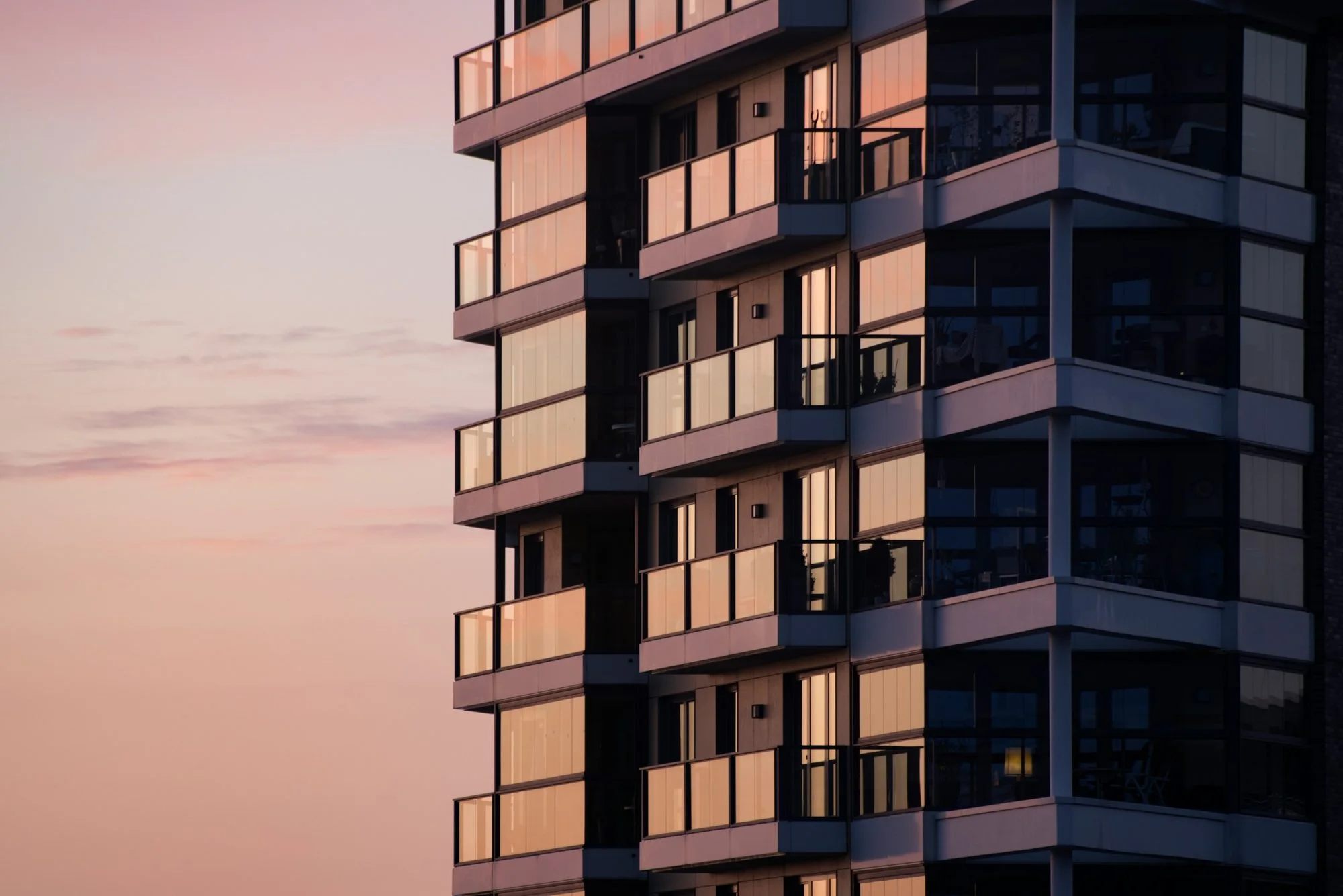 A residential tower with glass balconies at sunset